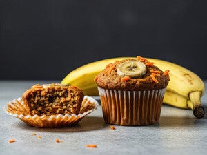 Banana muffin with sliced banana on top, next to peeled muffin and bananas.