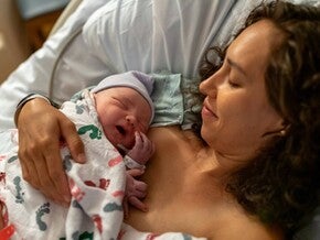 Fotografía: madre en hospital sosteniendo piel con piel a recién nacido con gorro y manta
