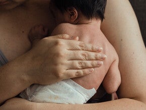 Mano adulta sosteniendo la mano minúscula de un bebé prematuro. Cuidado piel con piel (método canguro). Tono íntimo y sensible, luz cálida y tenue. Sin logos.