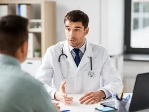 Photograph of a doctor in white coat speaking with a seated patient in an exam room
