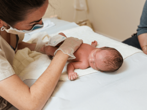 Photograph of a nurse examining a newborn on a white hospital changing table.