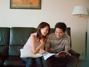 Photo of two people on a couch, smiling and reading a magazine