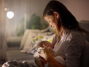 Madre meciendo a bebé en brazos en una habitación poco iluminada.