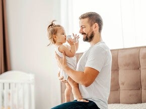Fotografía: padre sonriente sostiene a su hija pequeña en habitación luminosa