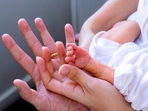 Mano adulta sosteniendo la mano minúscula de un bebé prematuro.