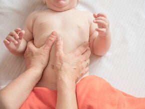 Mano de adulto haciendo masaje suave en barriga de bebé tumbado.