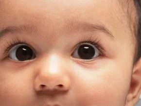 Close-up photograph of a wide-eyed baby with brown eyes and long lashes