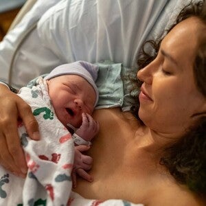 Fotografía: madre en hospital sosteniendo piel con piel a recién nacido con gorro y manta