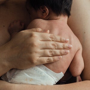 Mano adulta sosteniendo la mano minúscula de un bebé prematuro. Cuidado piel con piel (método canguro). Tono íntimo y sensible, luz cálida y tenue. Sin logos.