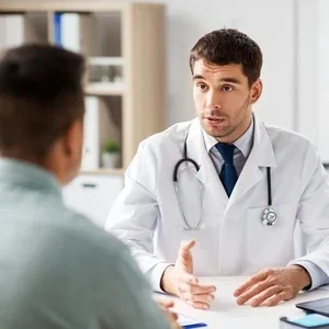 Photograph of a doctor in white coat speaking with a seated patient in an exam room