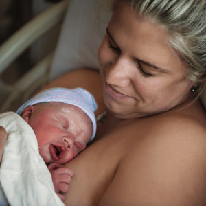 New mother cradling newborn against her chest, baby swaddled and crying