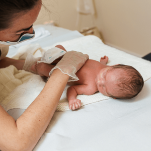 Photograph of a nurse examining a newborn on a white hospital changing table.
