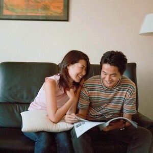 Photo of two people on a couch, smiling and reading a magazine