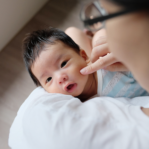 Photograph: newborn cradled on adult's shoulder, parent gently touching cheek
