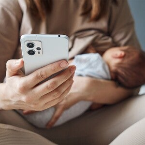Fotografía de persona con móvil sosteniendo a un bebé dormido