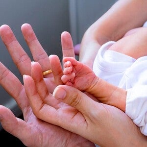 Mano adulta sosteniendo la mano minúscula de un bebé prematuro.