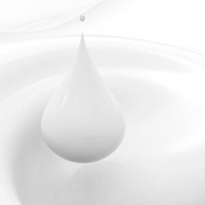 Detalle macro de una gota de leche cayendo sobre superficie blanca.