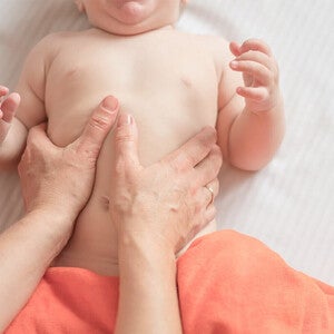 Mano de adulto haciendo masaje suave en barriga de bebé tumbado.