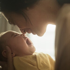 Madre con bebé en brazos junto a una ventana, mirándolo con calma. Luz natural suave, tono científico accesible. Sin biberón ni producto visible, sin logos.