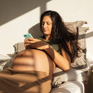 Fotografía: mujer en cama usando móvil, sombras de persiana