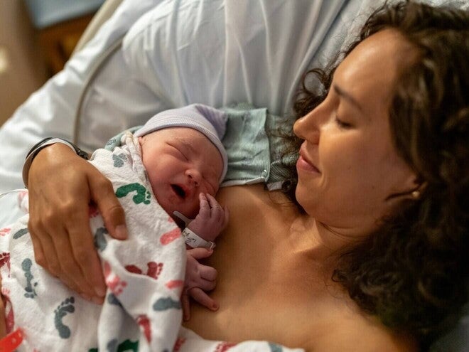 Fotografía: madre en hospital sosteniendo piel con piel a recién nacido con gorro y manta