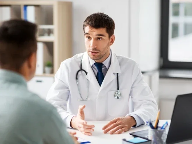 Photograph of a doctor in white coat speaking with a seated patient in an exam room