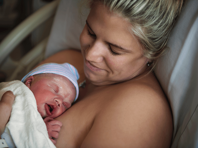 Photograph: mother cradling crying newborn skin-to-skin, tender gaze.
