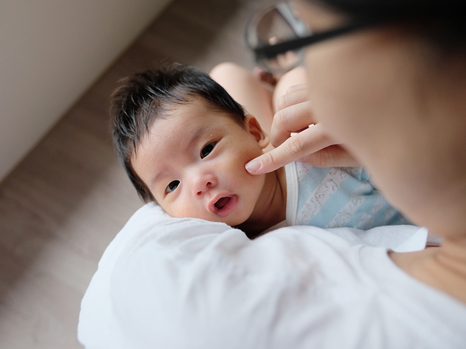 Photograph: newborn cradled on adult's shoulder, parent gently touching cheek