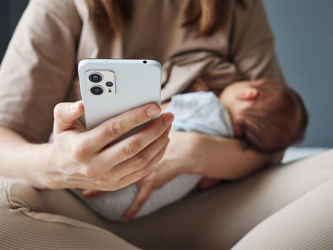 Fotografía de persona con móvil sosteniendo a un bebé dormido