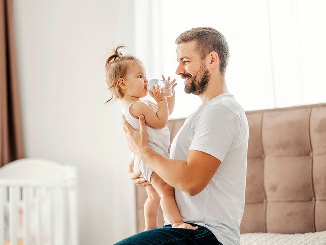 Fotografía: padre sonriente sostiene a su hija pequeña en habitación luminosa