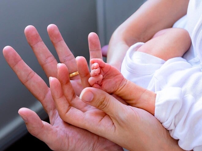 Mano adulta sosteniendo la mano minúscula de un bebé prematuro.