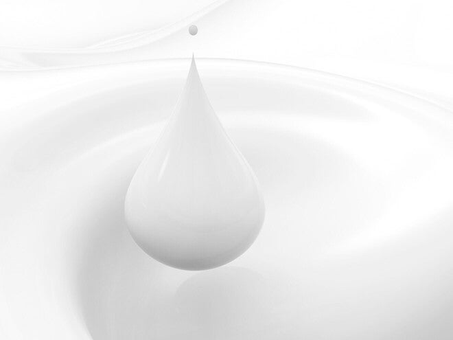 Detalle macro de una gota de leche cayendo sobre superficie blanca.