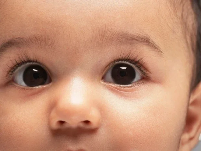 Close-up photograph of a wide-eyed baby with brown eyes and long lashes