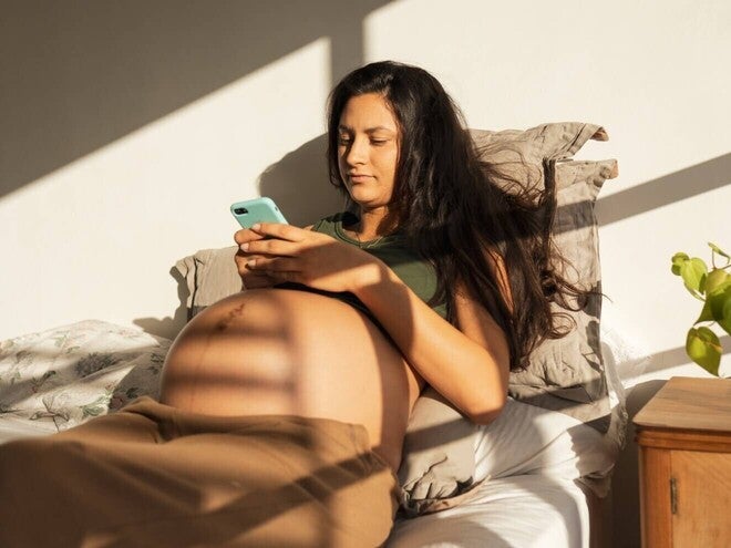 Fotografía: mujer en cama usando móvil, sombras de persiana