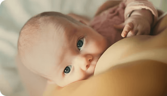 Un bebé de ojos azules está mamando, mirando hacia arriba mientras está acostado en los brazos de su cuidador.