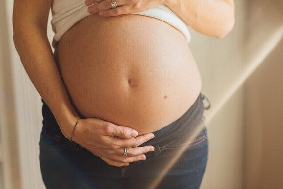 Fotografía de vientre de mujer embarazada, manos sosteniéndolo, luz cálida