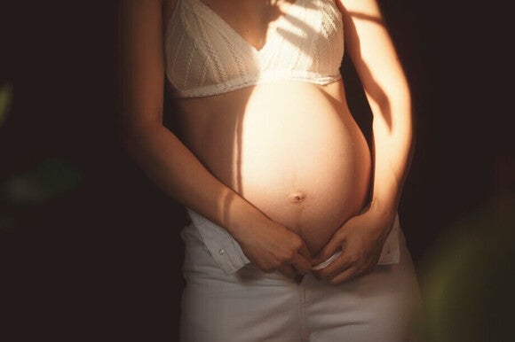 Fotografía de mujer embarazada con manos en forma de corazón sobre el vientre